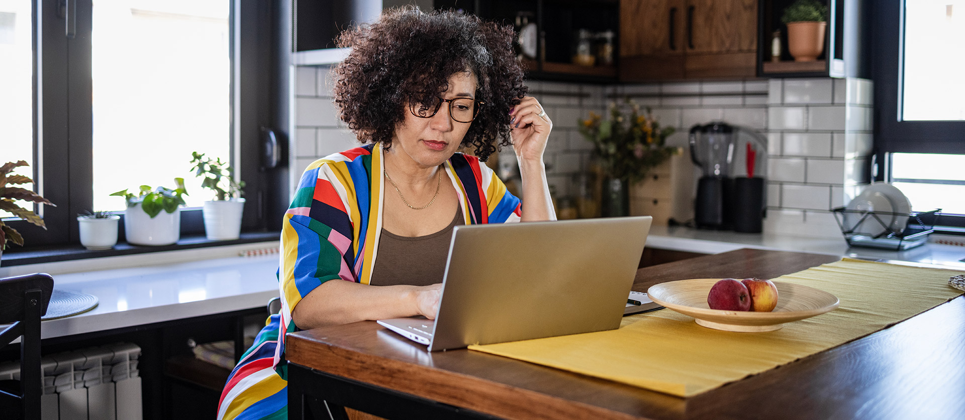 Een vrouw zit aan de keukentafel achter haar laptop